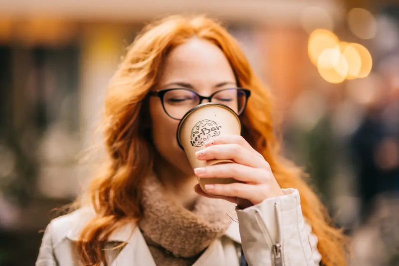 Commercial photography for a coffee shop. Happy lady drinking takeaway coffee on the street