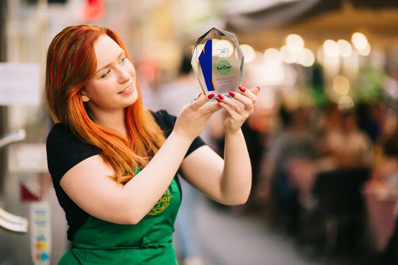 A HerBar waitress proudly showing their trip advisor award